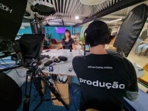 Equipe de produção grava vídeo com apresentadora em estúdio profissional, rodeada de equipamentos tecnológicos.