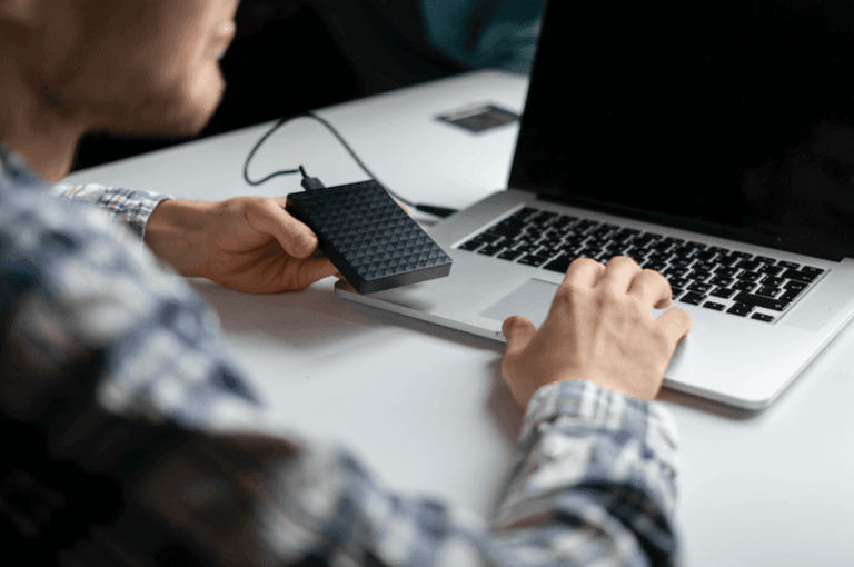 Usuário conectando um disco rígido externo a um laptop em uma mesa.