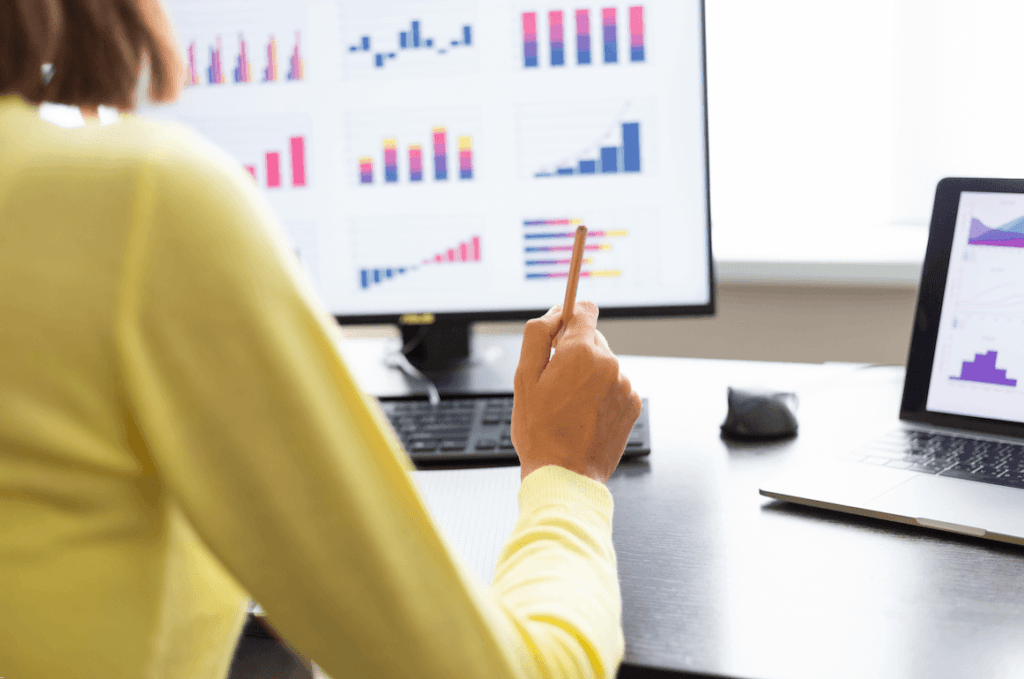 Profissional analisando gráficos de dados em dois monitores em escritório moderno.
