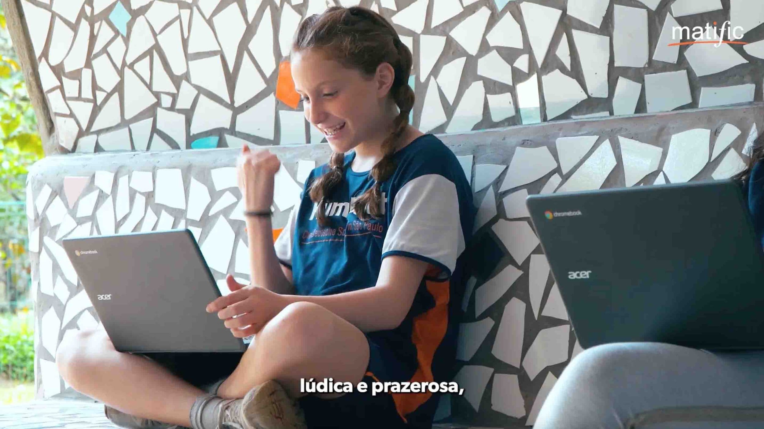 Jovem estudante sorrindo enquanto usa laptop Acer em ambiente escolar, divertido e acolhedor.