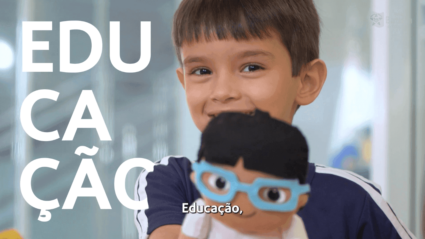 Criança sorrindo segurando boneco, com a palavra Educação ao lado. Ambiente educacional e divertido.