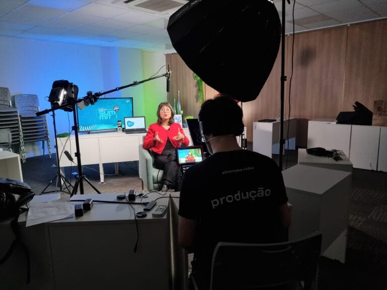 Mulher em palestra sendo filmada para o evento Dev Summit, com iluminação e equipamentos de produção.