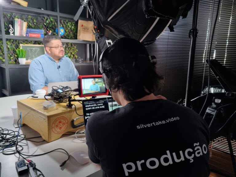 Entrevista em estúdio de gravação com técnico operando equipamentos de vídeo em frente a entrevistado.