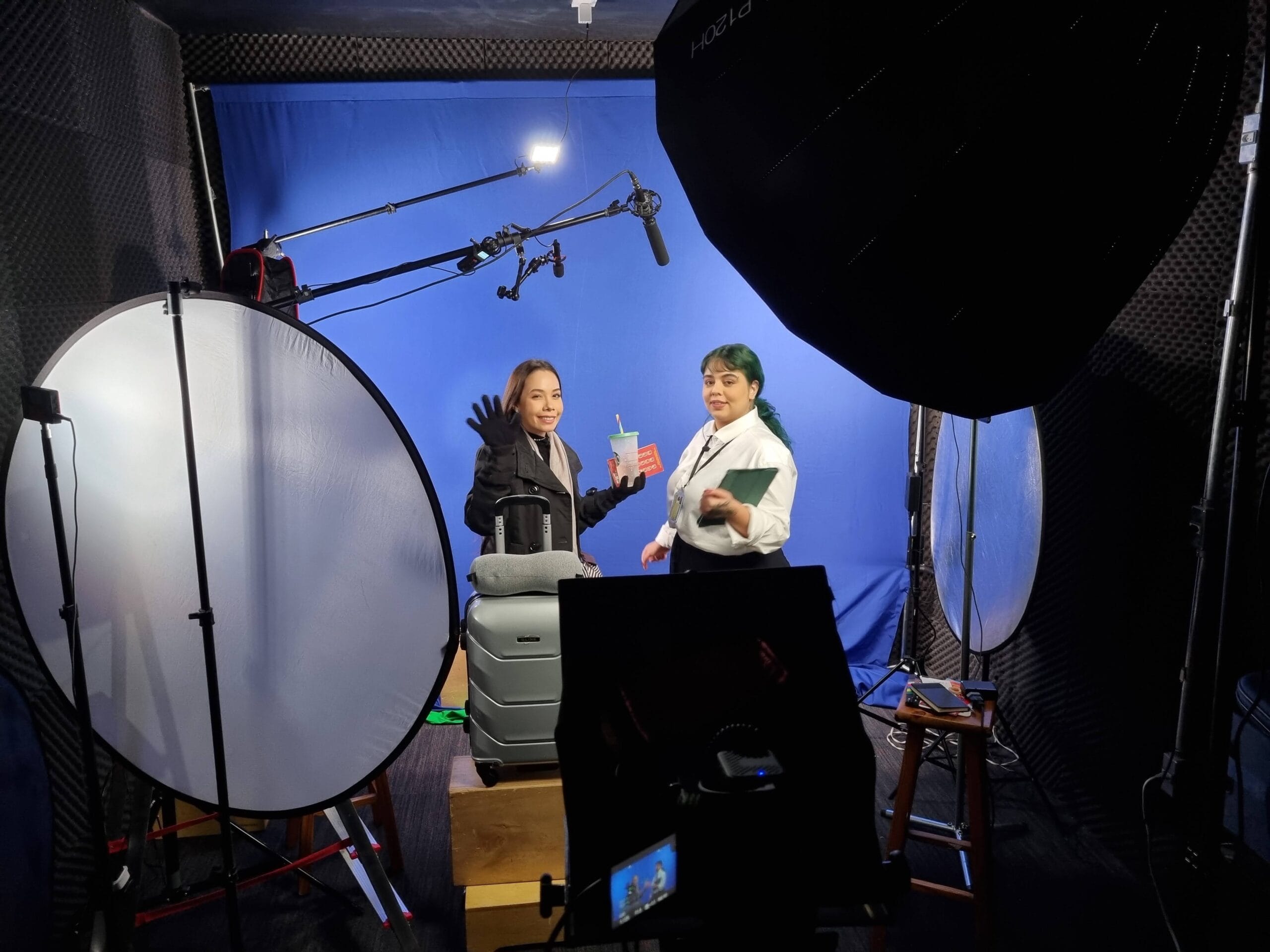 Duas pessoas em estúdio de gravação com equipamentos e iluminação, preparando-se para filmagem em fundo azul.