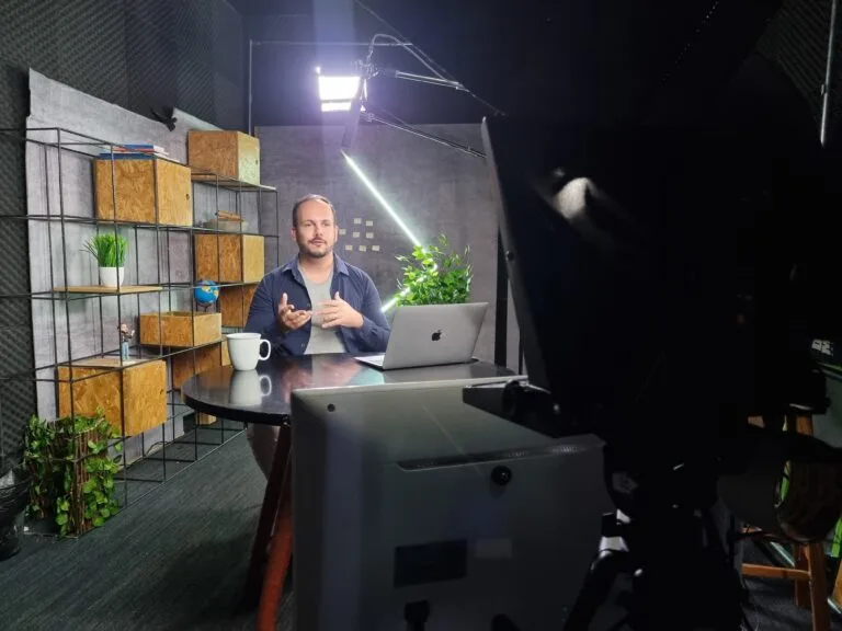 Homem gravando vídeo em home office com laptop, iluminação profissional e decoração minimalista.