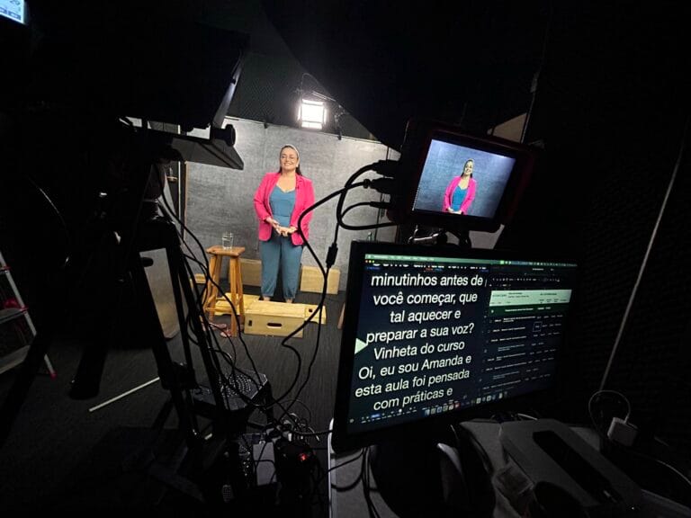 Mulher apresentando em estúdio com teleprompter e equipamentos de filmagem visíveis ao fundo.