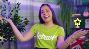 Pessoa sorrindo com camiseta verde letras em ambiente decorado, plantas ao fundo.