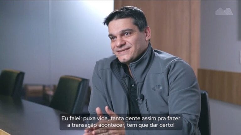 Homem sorrindo em reunião de negócios, expressão confiante. Legenda na imagem menciona importância do trabalho em equipe.