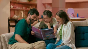 Família sorrindo enquanto lê livro juntos no sofá da sala, ambiente acolhedor e descontraído.