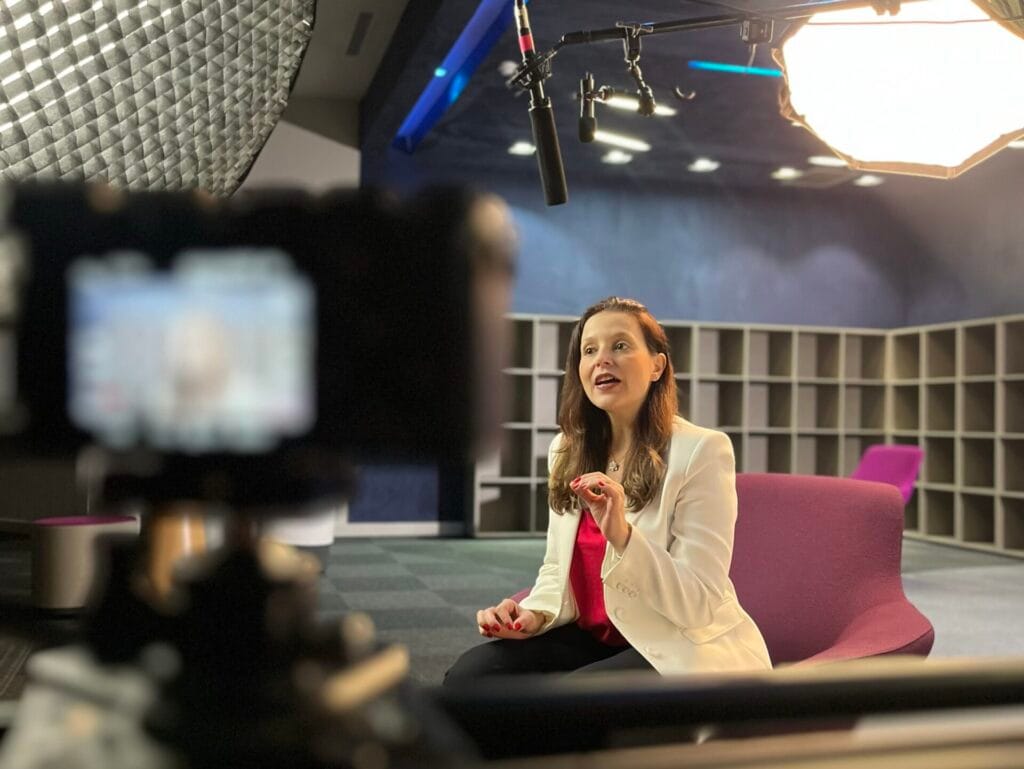 Pessoa dando entrevista em estúdio profissional, cercada por equipamentos de iluminação e gravação.
