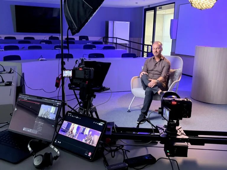 Gravação de entrevista em estúdio moderno, com equipamentos de vídeo e iluminação, e um apresentador sentado em uma cadeira.