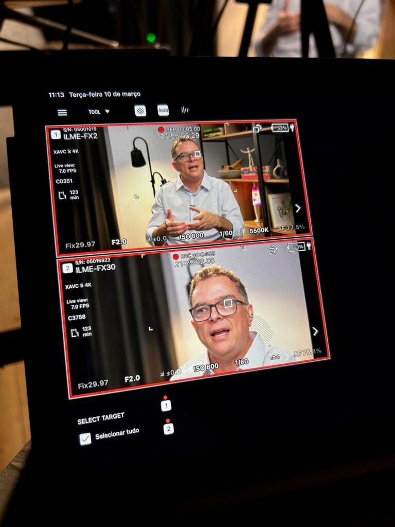 Monitor de vídeo mostrando duas tomadas simultâneas de um homem de óculos e camisa clara falando em um estúdio