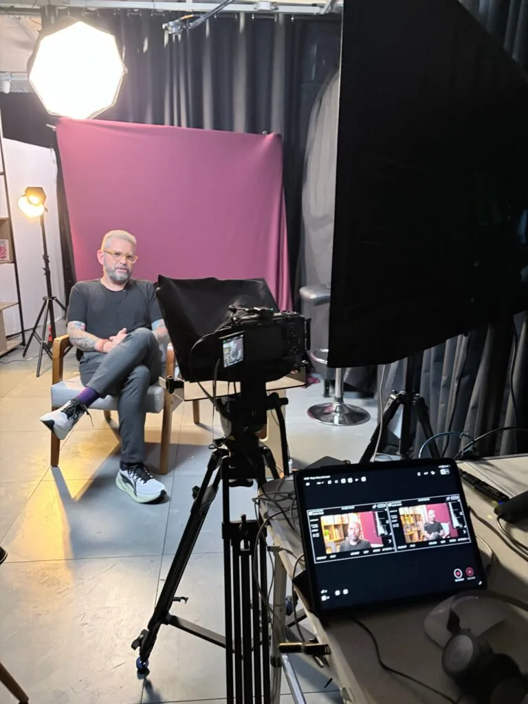 Gravando entrevista em estúdio com fundo roxo, câmera em destaque e iluminação profissional. Atmosfera criativa.