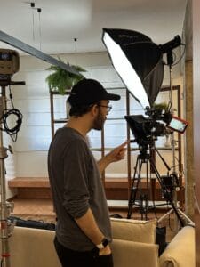 Cineasta ajustando equipamento de gravação em um estúdio, com iluminação e câmeras visíveis.