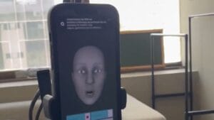 Alt text: Tela de smartphone exibindo uma face virtual em um ambiente de escritório com luz natural.