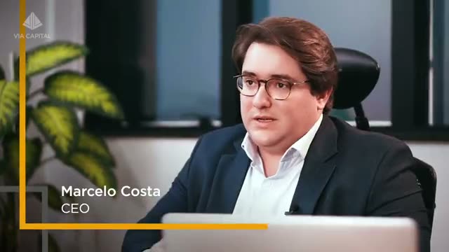 Marcelo Costa, CEO da Via Capital, conversando em escritório moderno, próximo a plantas e com laptop à frente.